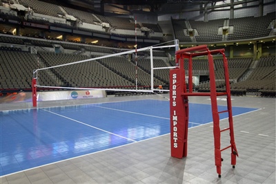 Indoor volleyball court with a grey and blue playing surface and a red referee stand.
