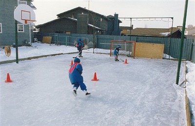 Outdoor hockey rink with hockey net and basketball hoop and kids doing hockey drills.