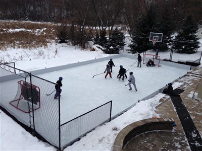 Outdoor hockey rink with hockey nets, a basketball hoop, with fences and hockey goals on each end in River Hills.
