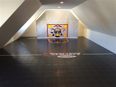 Indoor hockey practice area with black flooring, a hockey net, and a central logo.