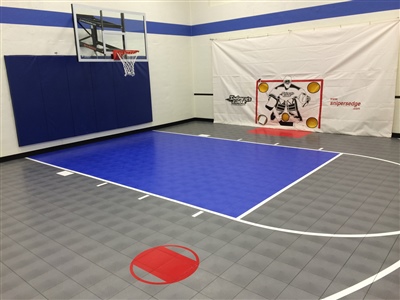 Indoor sports court with grey flooring, blue and red key areas, with a basketball hoop and hockey goal. 