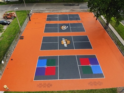 Multipurpose outdoor sport court with orange and black flooring, with tennis courts, hopscotch, and a basketball court.