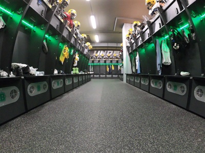 Grey flooring for a teams locker room with multiple lockers lining the room. 