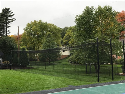 Outdoor batting practice area on grass with black netting surrounded by trees. 