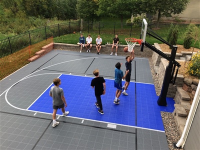Outdoor residential basketball court with a gray and blue surface with white and black lines in Madison.