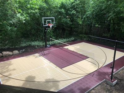 Outdoor residential basketball court with a maroon and yellow surface, a U of M logo in the center, and two basketball hoops.