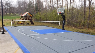 Outdoor residential sports court with a gray and blue surface, featuring a basketball hoop and a volleyball net in Lake Genova.