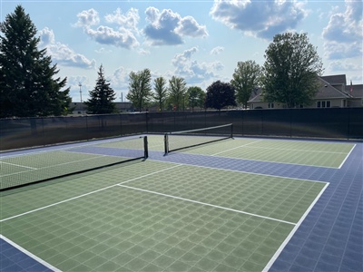 Outdoor sports court with a green and blue surface, white lines, and a tennis net in River Hills.