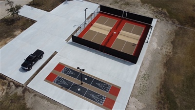 Outdoor sports area with two sections: one with a beige and red surface housing two tennis courts and one with multiple shuffle boards for multipurpose uses in River Hills.