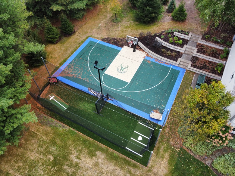 Aerial view of a Bucks-themed backyard multi-sport court, batting cage and retaining wall in Delafield, WI